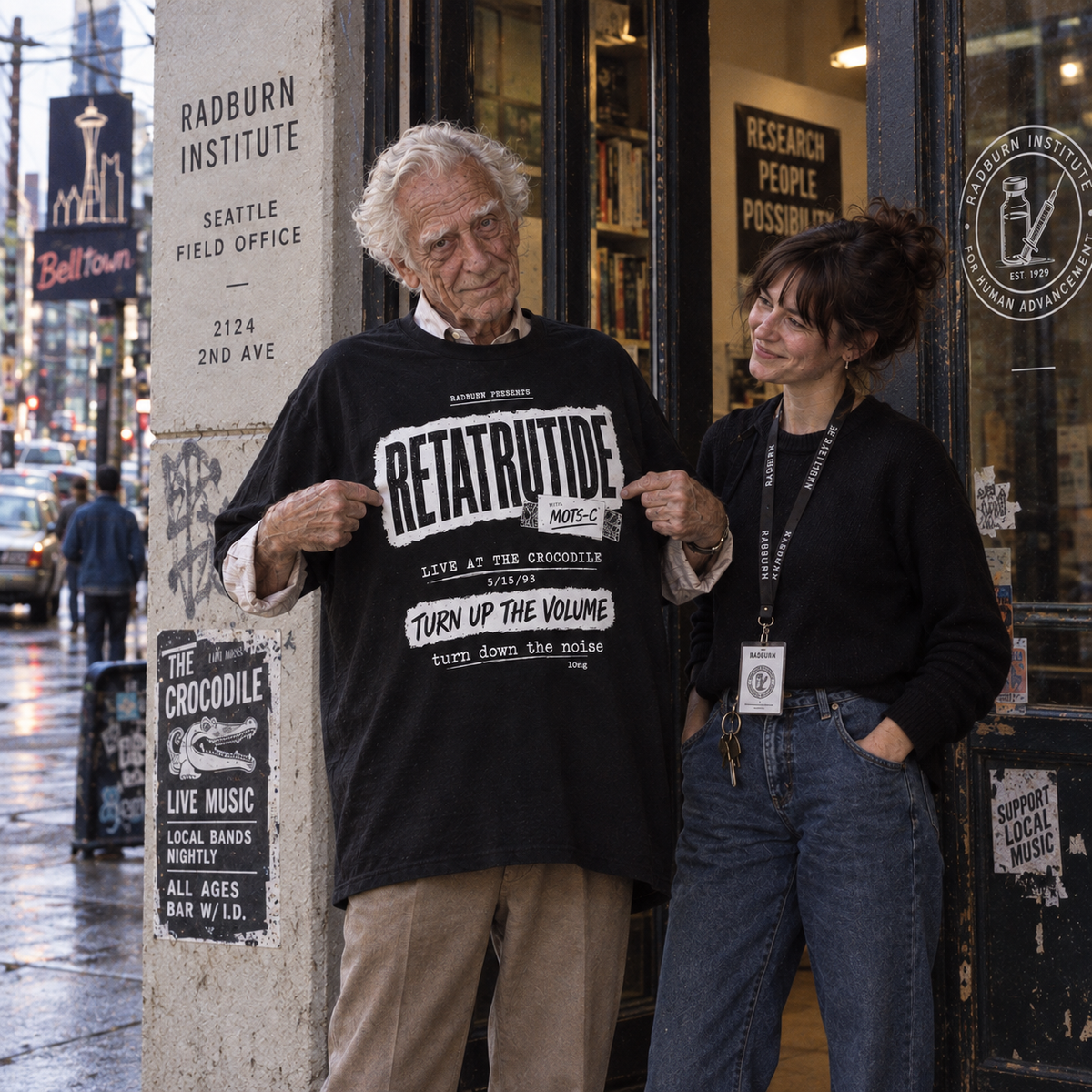 Older man displays a black Retatrutide shirt beside a woman outside a storefront | color:Black